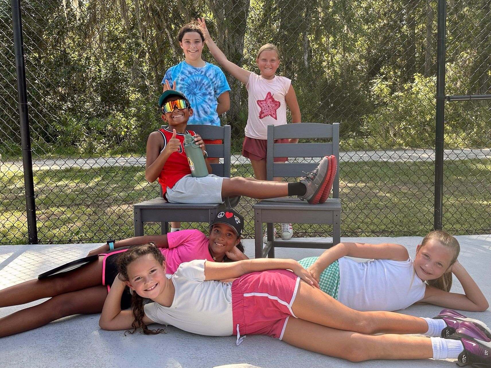 Six students relax together on and around a courtside bench between sessions, some sitting, some lying on the ground.