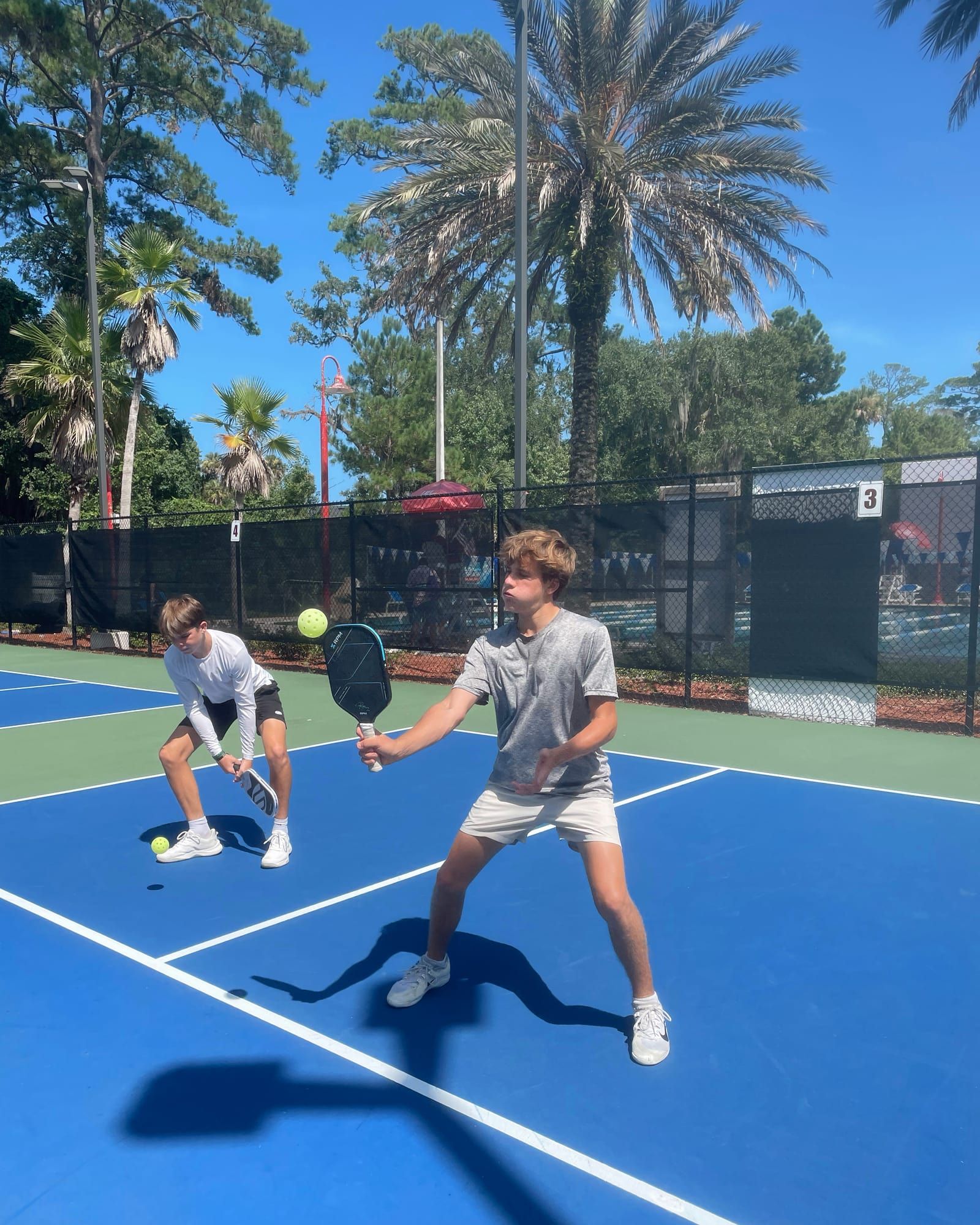 One young player lunges to reach a low ball while their partner holds position further back on the blue court.