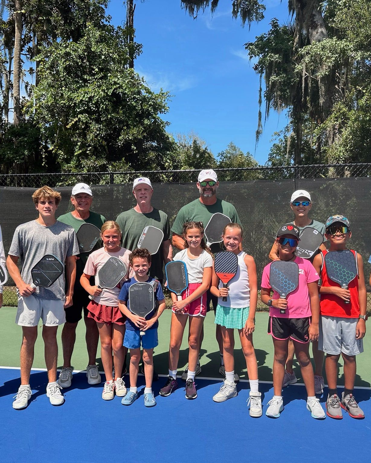 The full session group — around a dozen students with their coaches — lined up across the court holding paddles for a team photograph.
