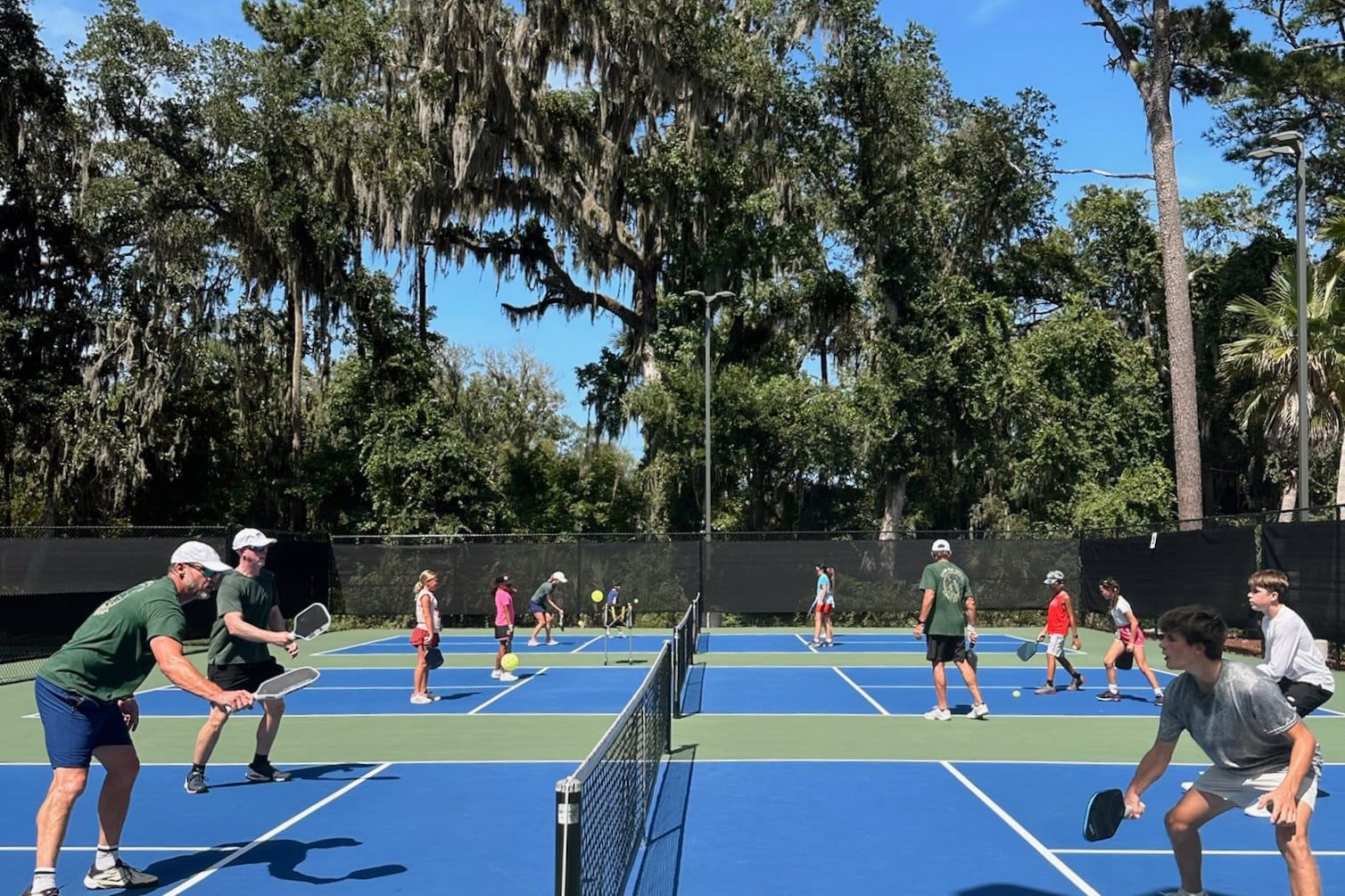 A coach demonstrates a swing on the near court while students play on the courts beyond.